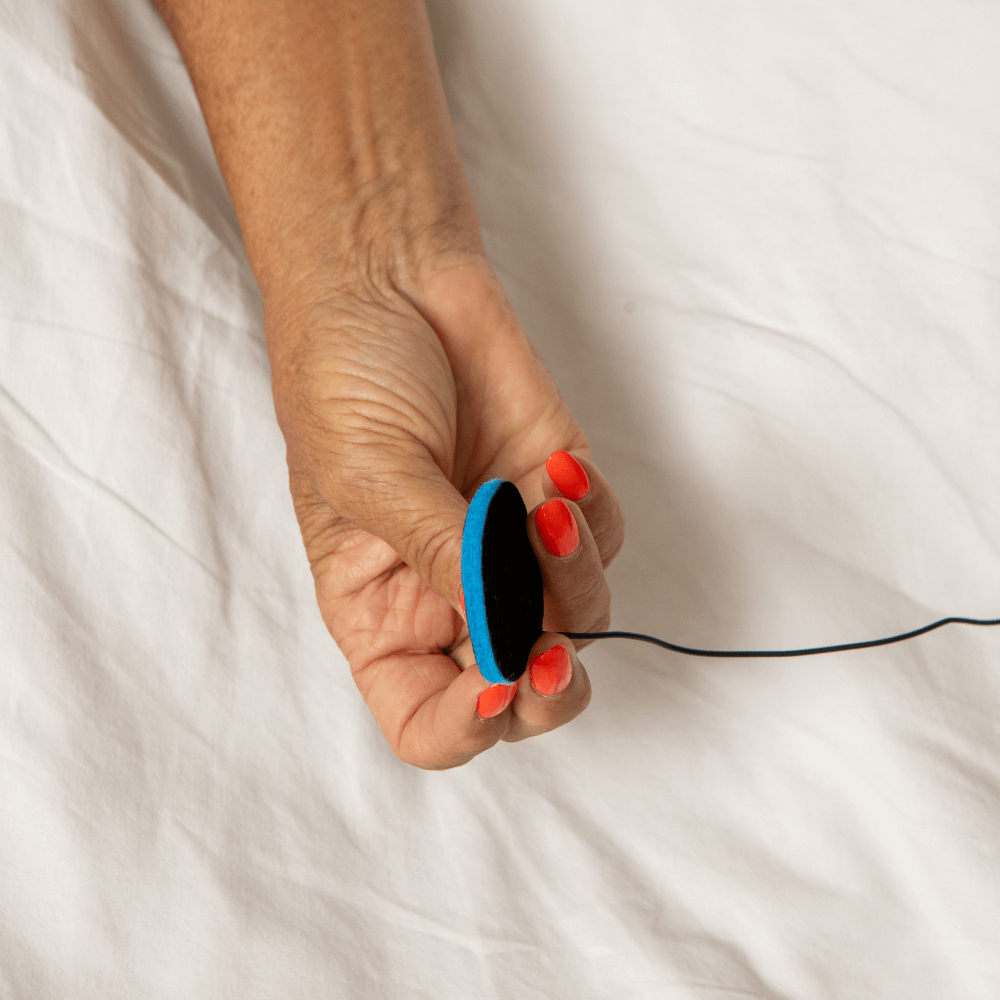 Hand holding a very thin speaker thats soft material and blue and black with a cable to the sleep mask where you can listen to sounds